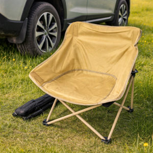 Beige foldable camping chair placed outdoors next to a car in a green field.