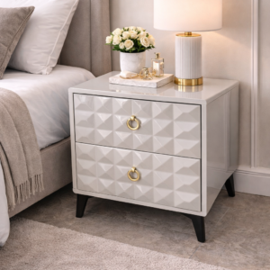 Modern white bedside table with geometric drawers, gold handles, and black legs in a stylish bedroom setup.
